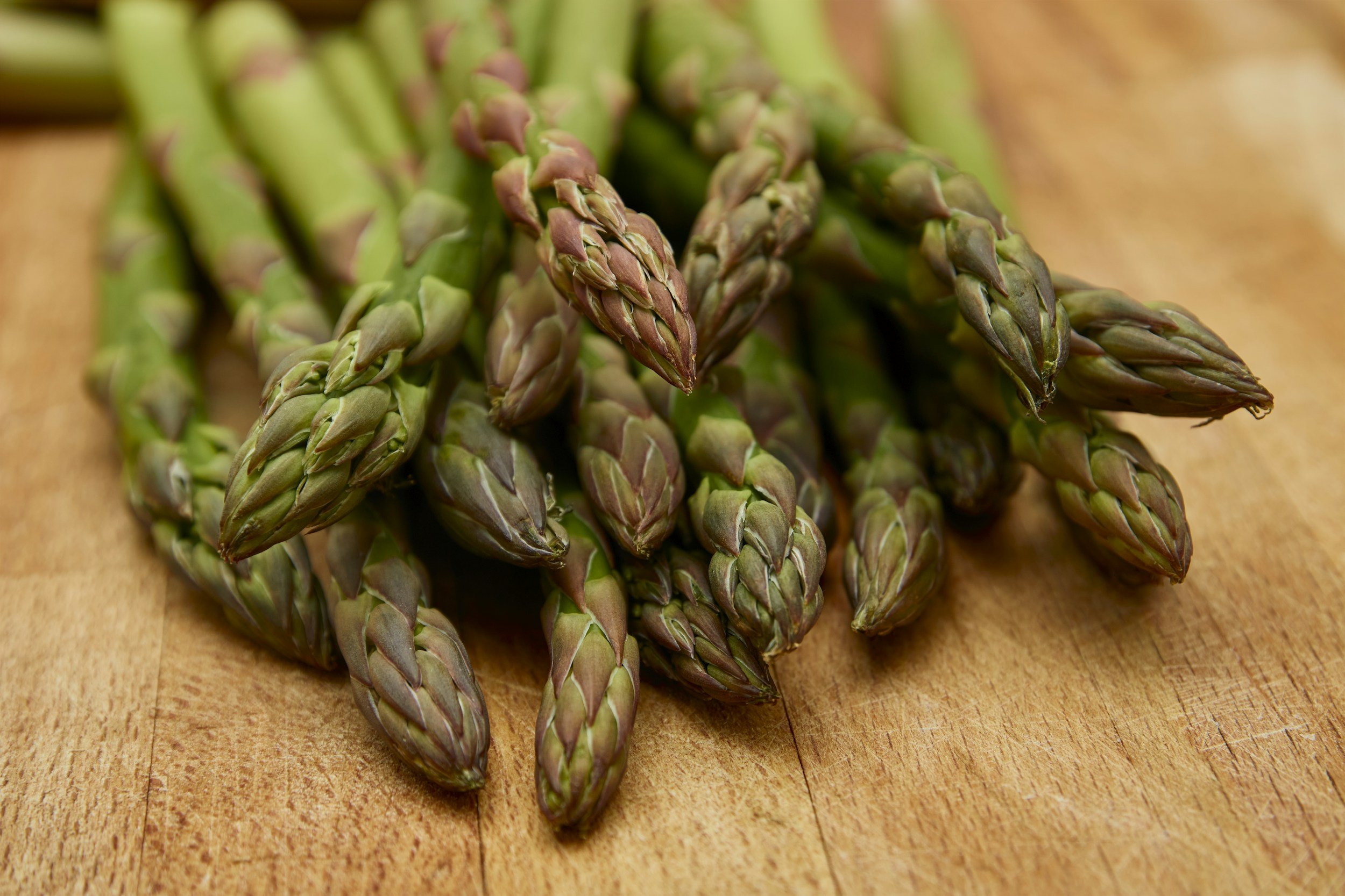 unsplash-image-36u1qSdwjsI Fresh green asparagus spears arranged on a wooden surface, showcasing their vibrant color and unique texture, ideal for healthy recipes and culinary presentations.